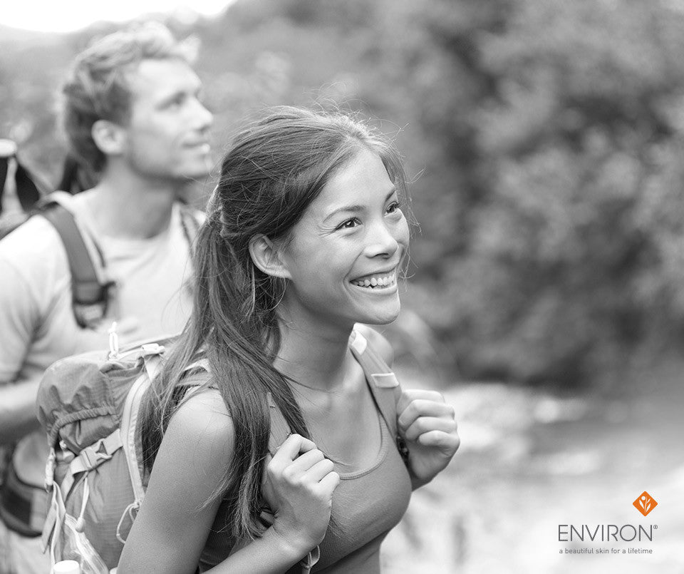 Black-and-white photo of a smiling woman with long ponytail wearing sleeveless top and backpack in beauty article