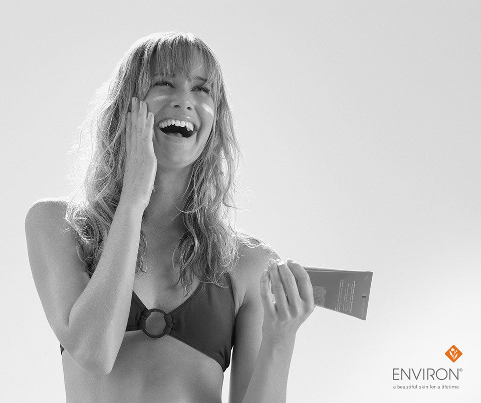 A woman in a bikini holds a tube of Environ sunscreen highlighting life-changing sun protection benefits.