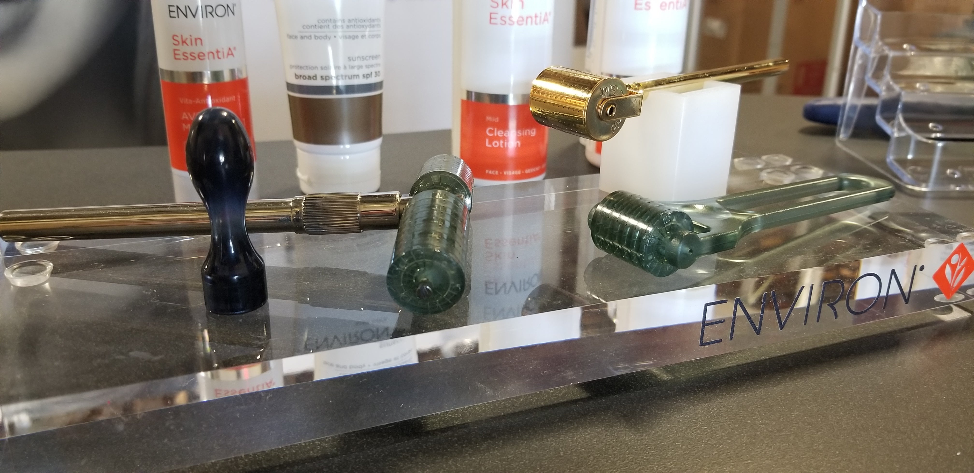 Gold-toned derma roller with black handle and green translucent head on acrylic tray for cosmetic microneedling use