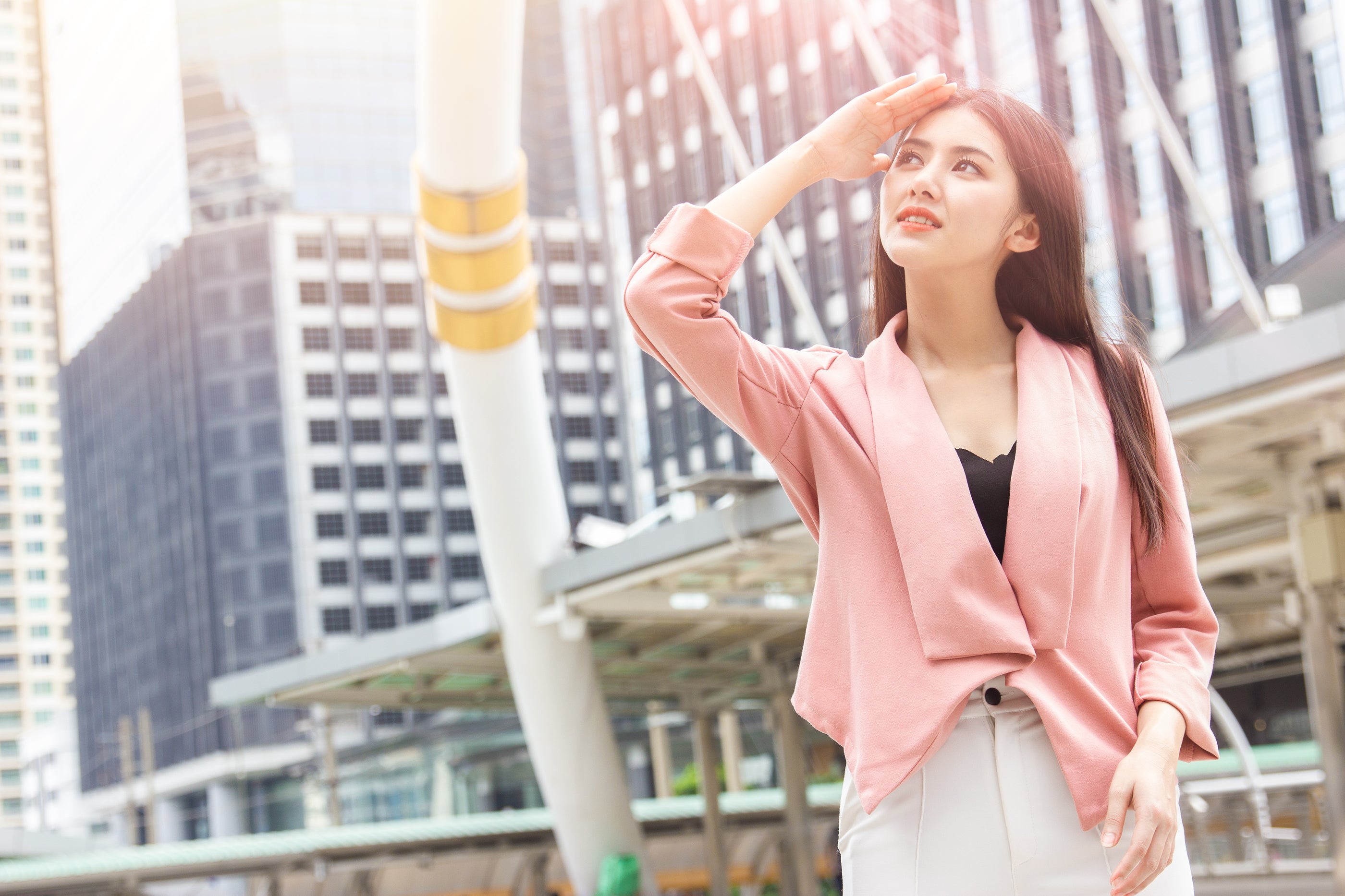 A woman wearing a soft pink tailored blazer over a black top and gray trousers in an article on saving skin from pollution