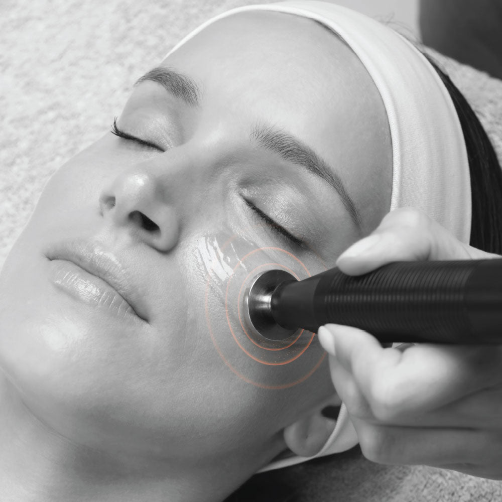 Black handheld microcurrent facial device with metallic tip used on cheek for ATP skin treatment benefits