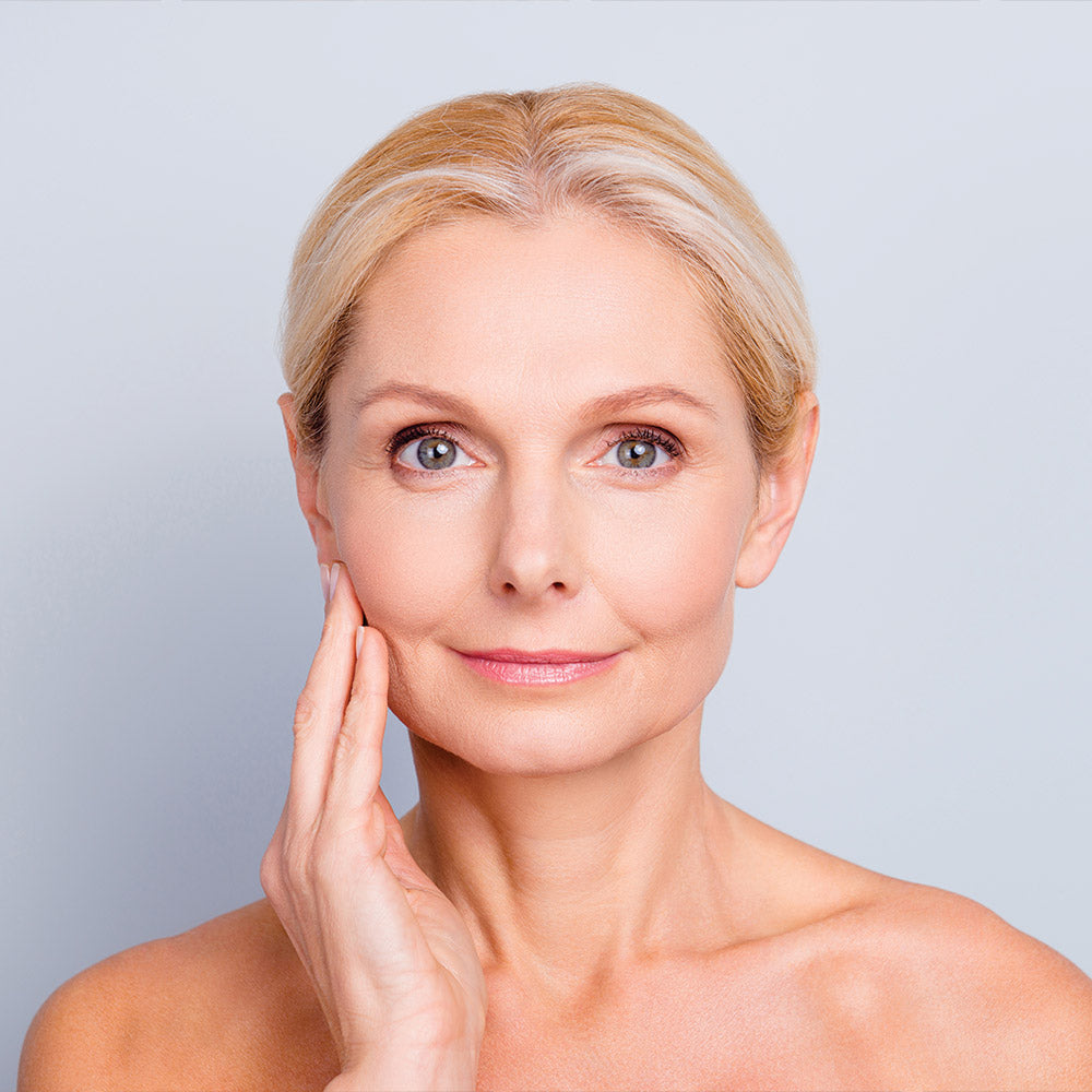 A woman with blonde hair and light-colored eyes gently touching her face addressing undereye concerns