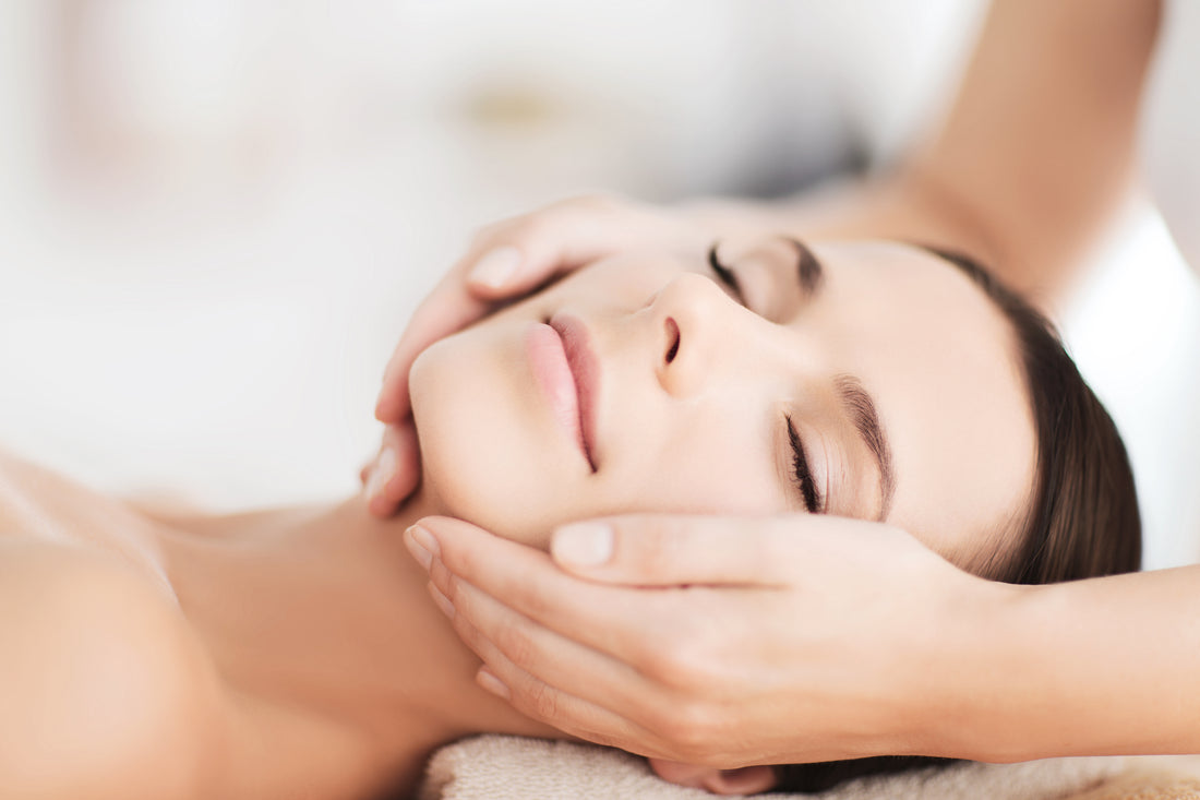 A woman receiving a facial massage with hands gently cradling her face in a cosmetic needling treatment session