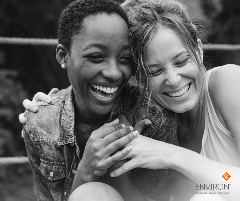 Black-and-white photo of two women laughing closely in denim jacket and sleeveless top for the article Heres to your health