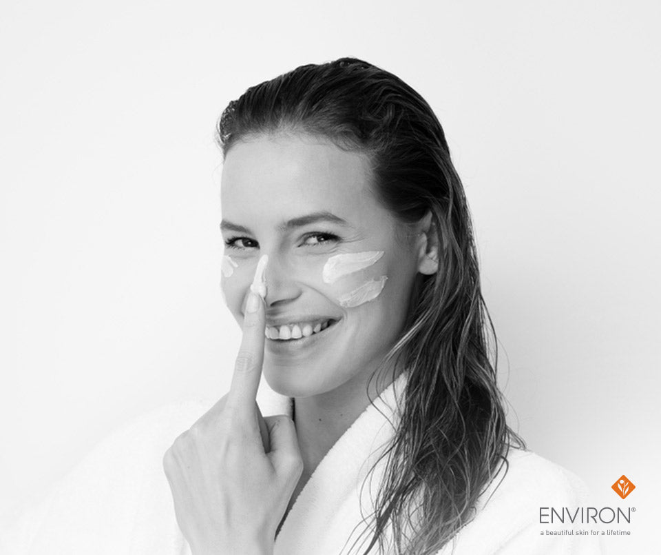 A woman wearing a white robe with cream-colored facial masks on cheeks and nose in an article about feeding your skin