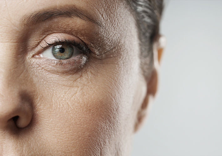 Close-up of a woman’s green eye with subtle makeup and natural skin texture illustrating aging eyes.