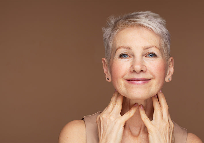 A woman with short silver hair and blue eyes gently touching her neck illustrating accelerated aging effects.