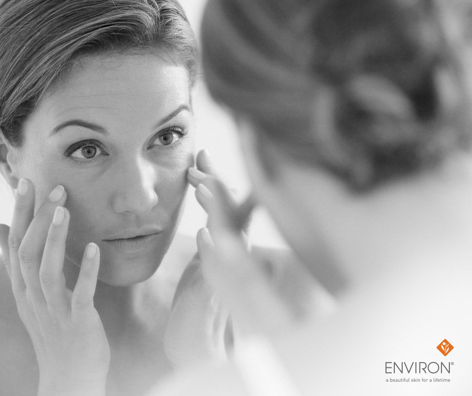 Black-and-white photograph of a woman gently touching her face while looking at herself in the mirror step it up