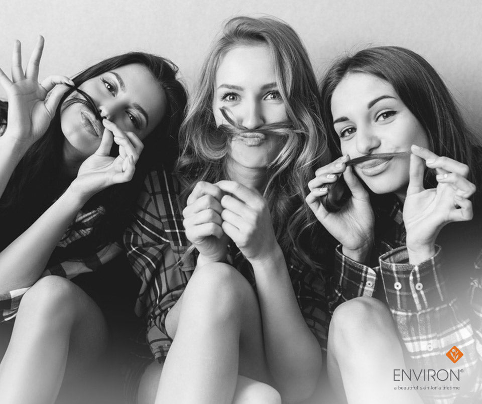 Black-and-white photo of three women playfully holding dark thin mustache props celebrating joy in new year resolution