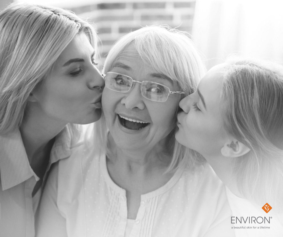 Black-and-white photo of an older woman with glasses kissed on both cheeks by two younger women for grandma’s beauty secrets article