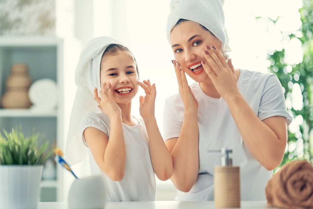 A woman and young girl wearing white towels apply vitamin A skincare products in a year-round routine.