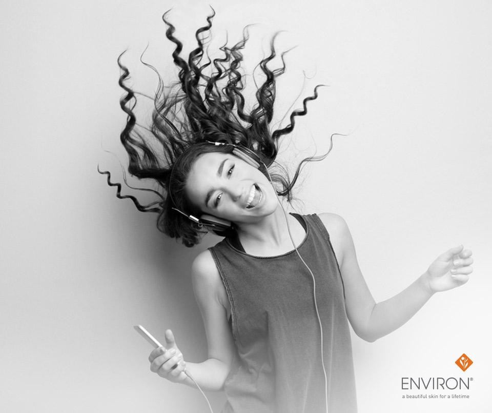 A woman with voluminous curly hair wearing black over-ear headphones holding a smartphone for energy boost tips