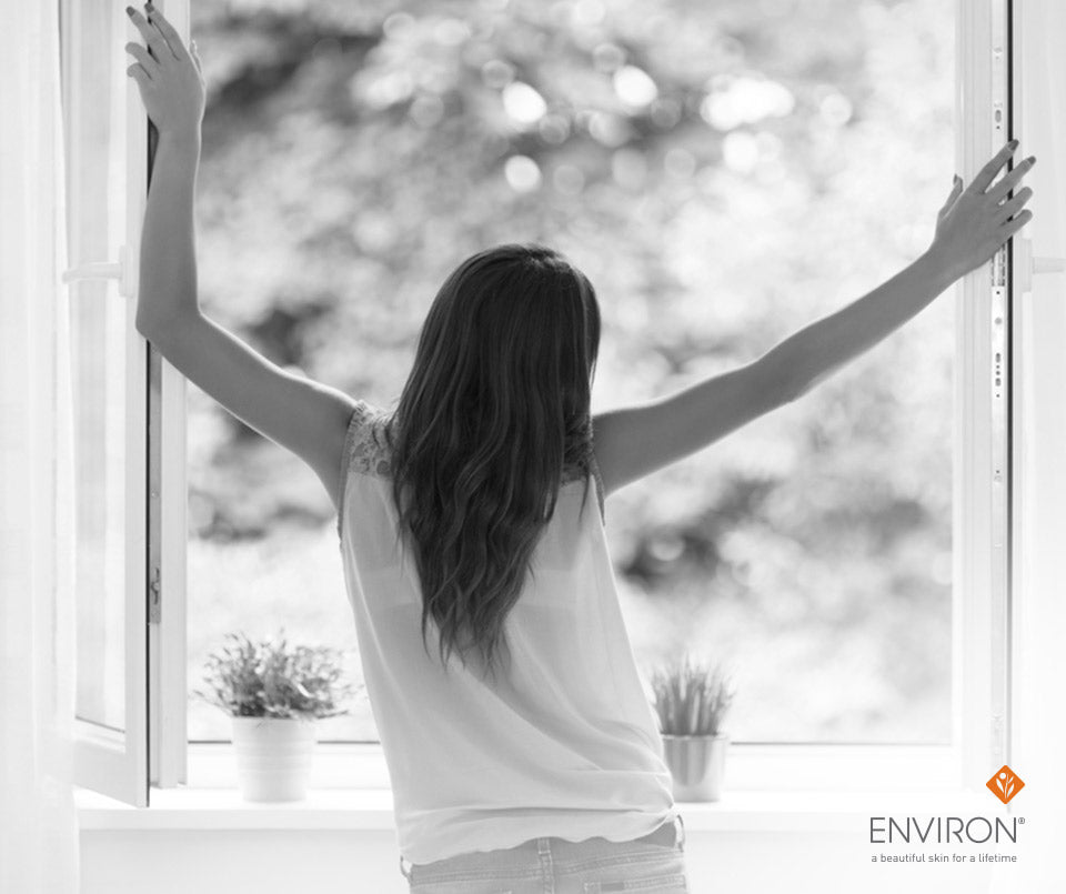 A woman with long dark hair stretches toward the light by a window in a moment of sublime summertime calm.