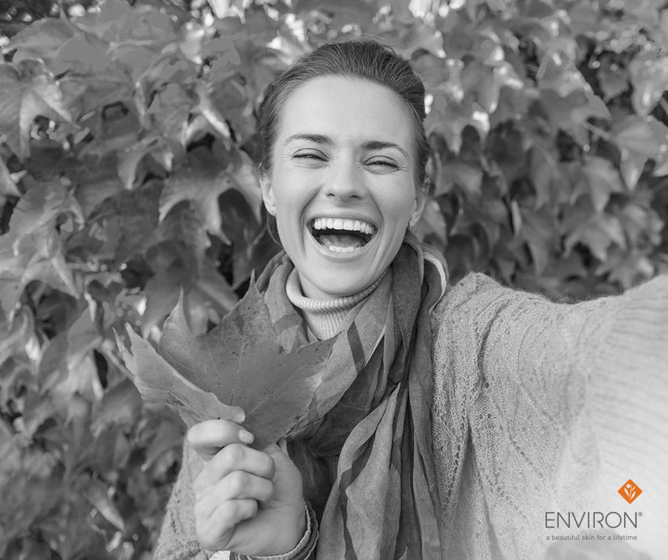 Woman wearing a textured cream knit sweater holding an autumn leaf in stress less for radiant skin article.