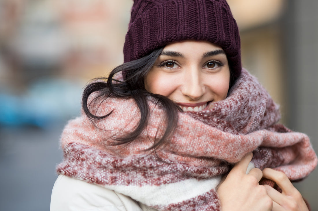 A cozy textured maroon and pink knit scarf wrapped warmly around a woman’s neck for fall skin care layers
