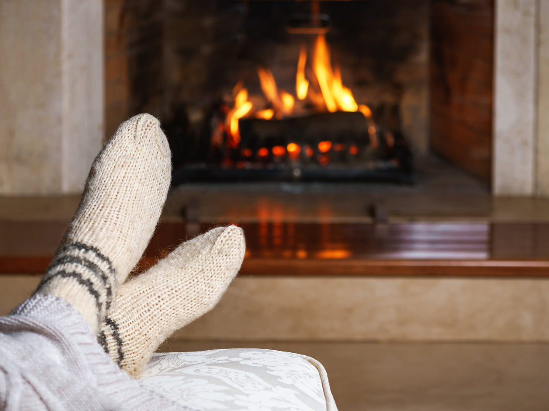 Cream-colored knitted socks with dark gray stripes near a fireplace for cozy winter hydration comfort