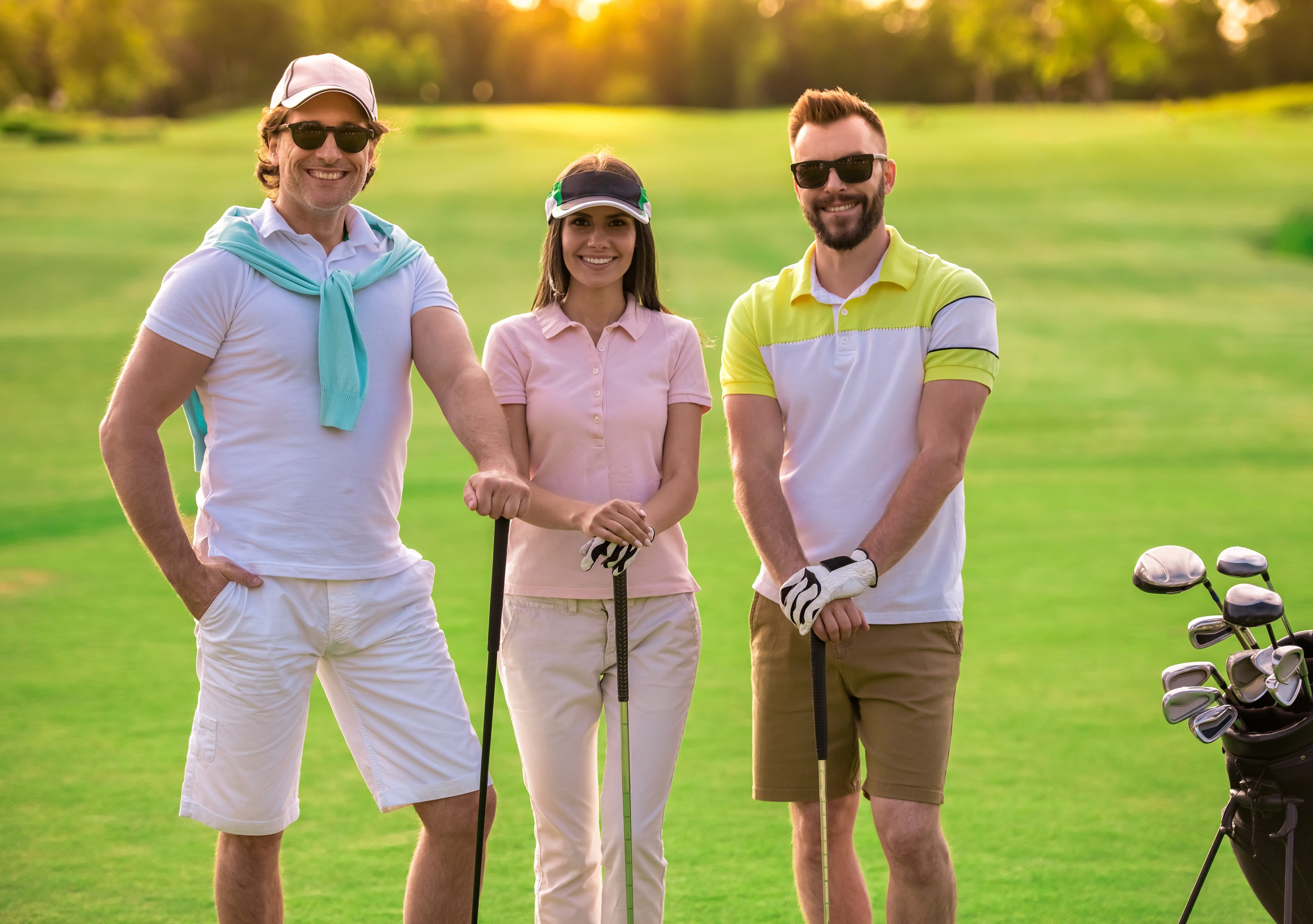 Three golfers on green course wearing sun care defense apparel including sunglasses, white cap, and pink and striped polos.