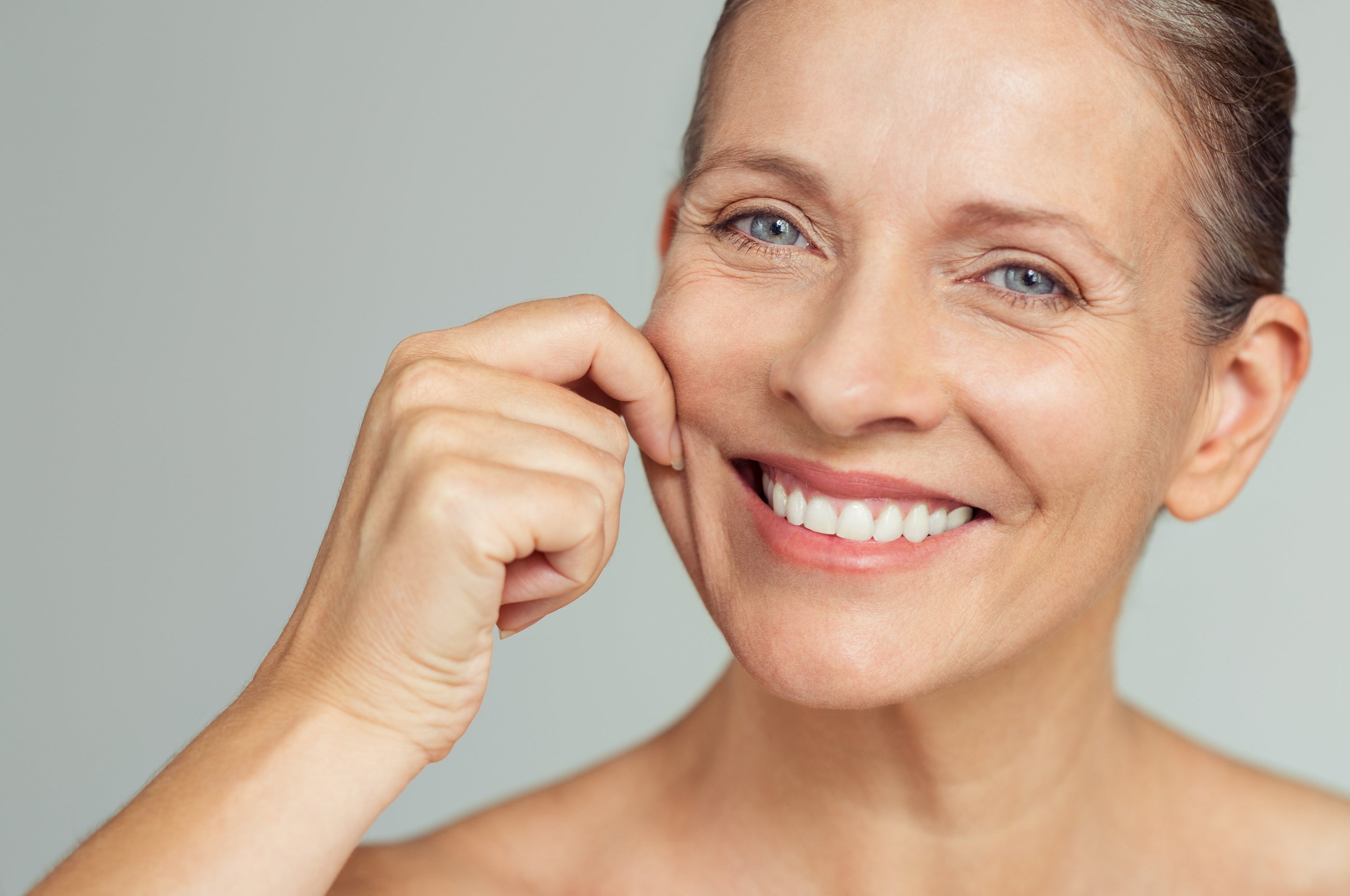 A woman with blue eyes and a warm smile showcasing healthy-looking skin in an article about skin care.