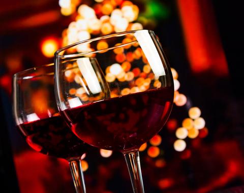 Two elegant clear glass wine glasses filled with deep red wine in a holiday skin care management setting