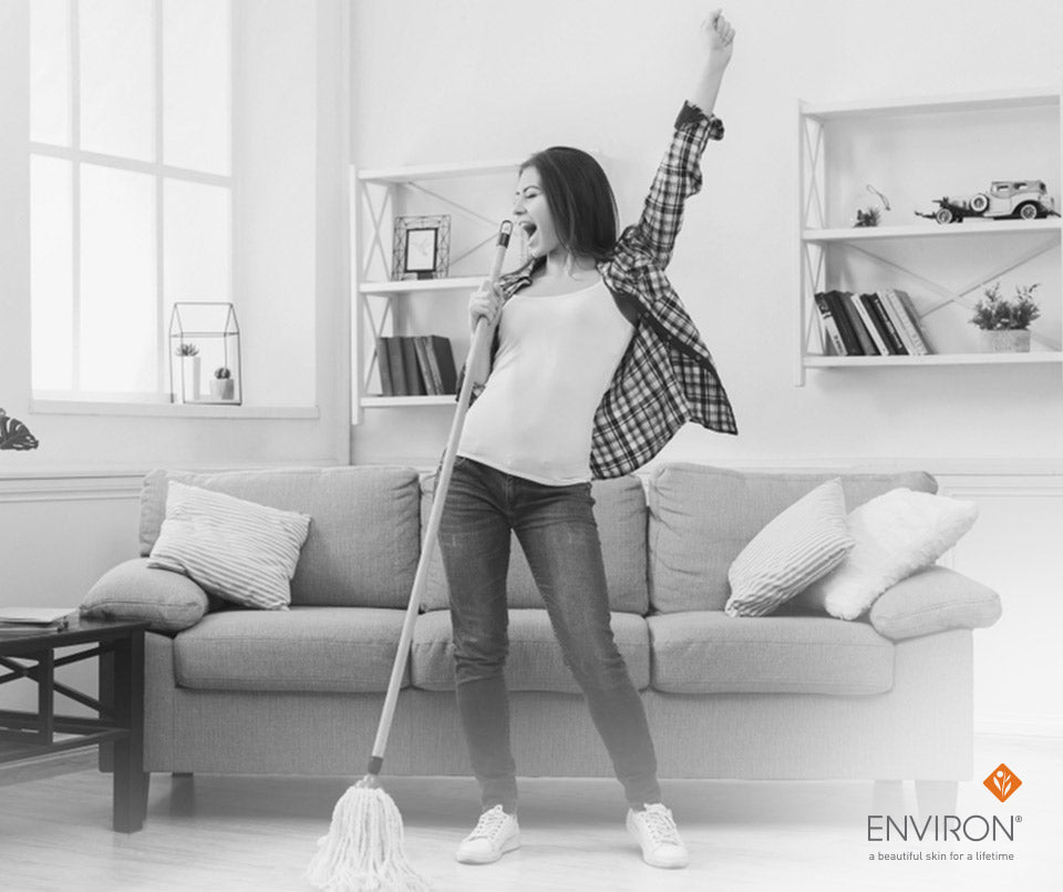 A woman in a plaid shirt and jeans joyfully holds a mop as a microphone in an organizing tips article.