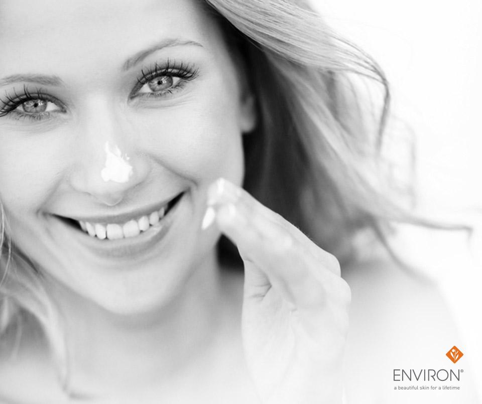 A woman with long wavy hair smiles while applying white sunscreen to her nose for skin cancer protection in may.