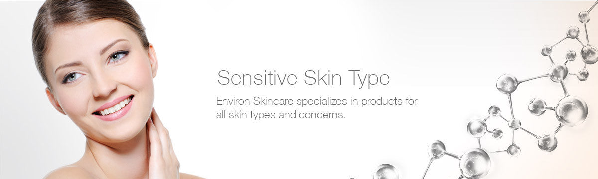 A woman with fair skin and brown hair smiles gently while touching her cheek in a sensitive skin collection.