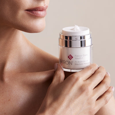 A sleek, transparent jar with a silver metallic lid and band holds the environ focus care youth+ tri biobotanical revival masque.