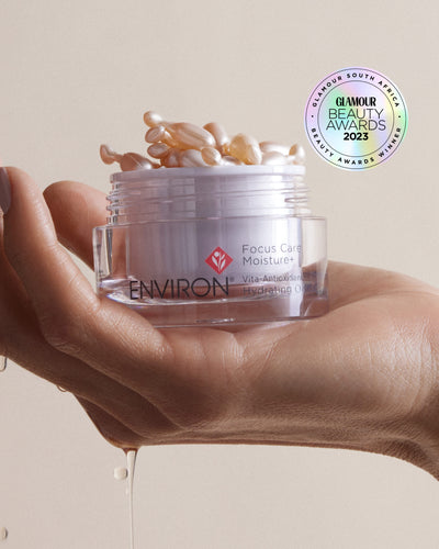 A clear glass jar of environ focus care moisture+ vita-antioxidant hydrating oil, filled with golden gel capsules and topped with a white lid.