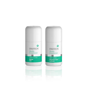 Two white bottles of Environ Body EssentiA skincare products, featuring Body Oil and Derma-Lac Lotion, stand side-by-side on a reflective white surface.