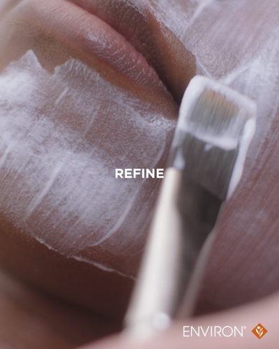 A white, textured facial mask being applied with a brush to the skin.