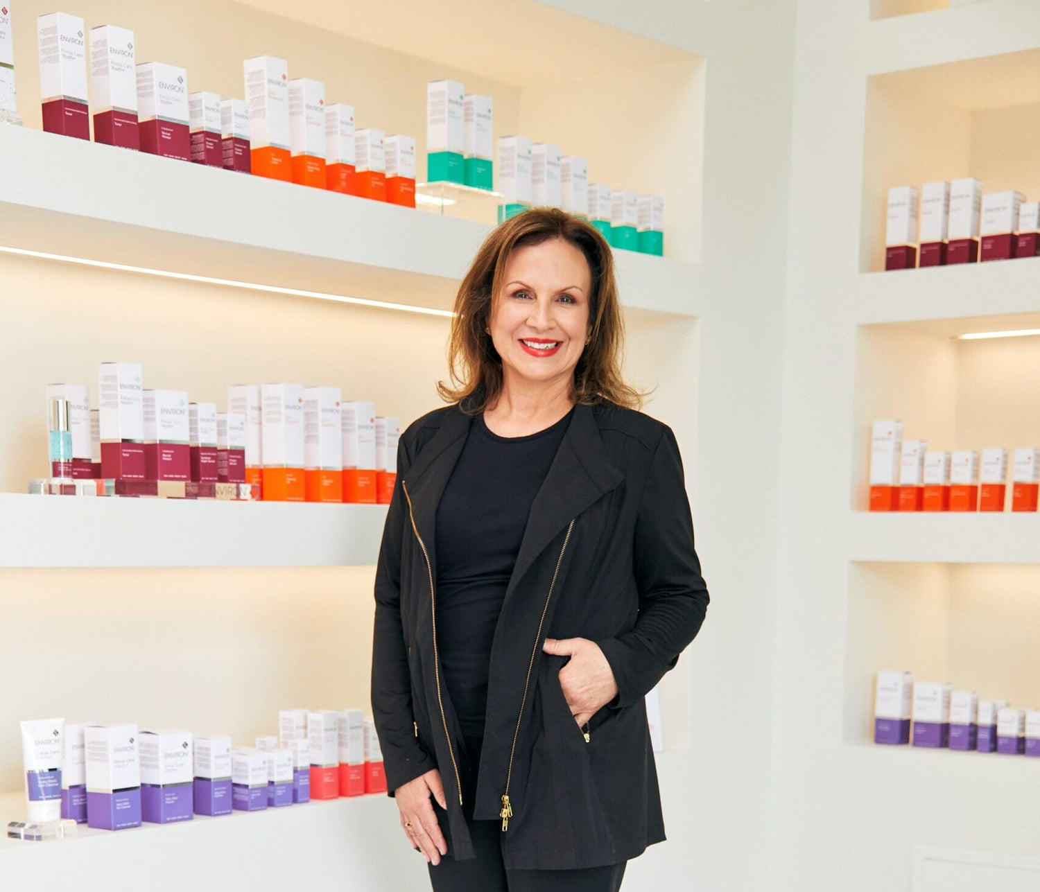 Woman in black blazer with gold zipper details standing before shelves of skincare products
