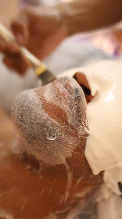 A person’s face covered in a white, foamy facial mask with visible droplets of liquid.
