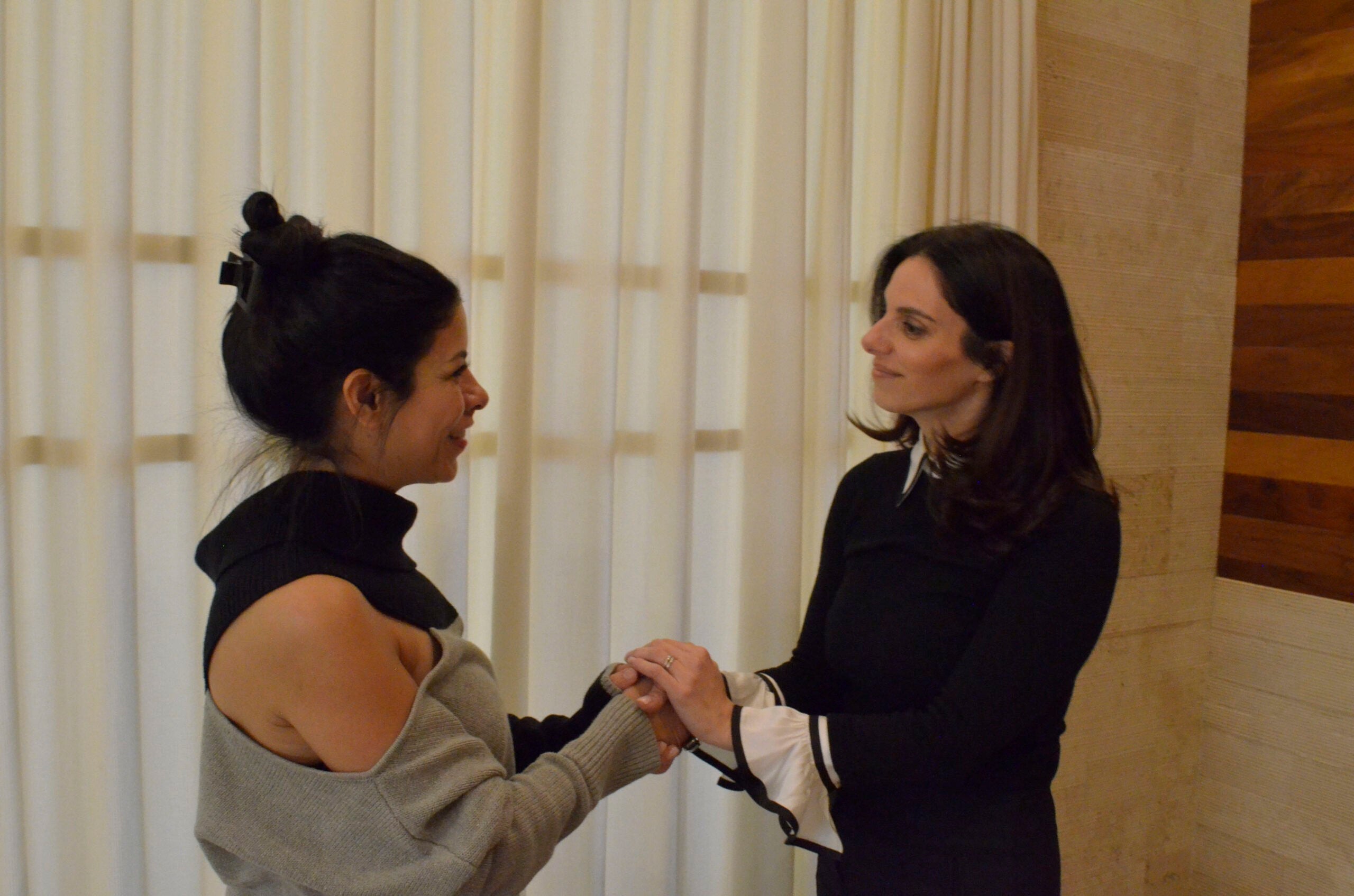 Two women in black and grey attire holding hands