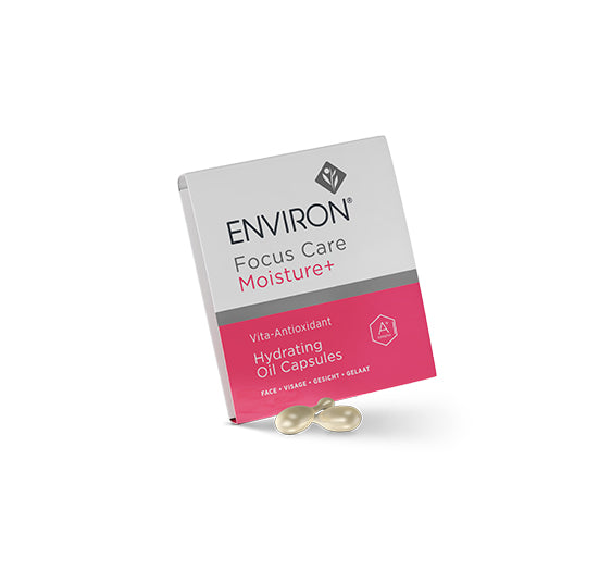 Two golden Environ Vita-Antioxidant Hydrating Oil Capsules sit in front of their signature white and pink Focus Care Moisture+ skincare box.