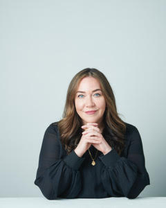 A woman with long brown hair wearing a black blouse.