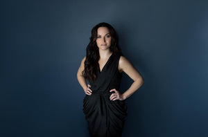 A woman wearing a sleek black sleeveless dress with a draped, asymmetrical design.