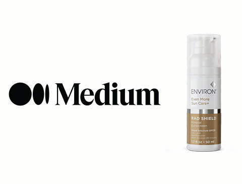 A sleek, transparent pump bottle with a white cap and brown label containing ’environ even more sun care’ sunscreen.