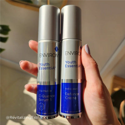 Two silver-topped, cylindrical bottles of environ youth essentia skincare products with blue labels and white text.