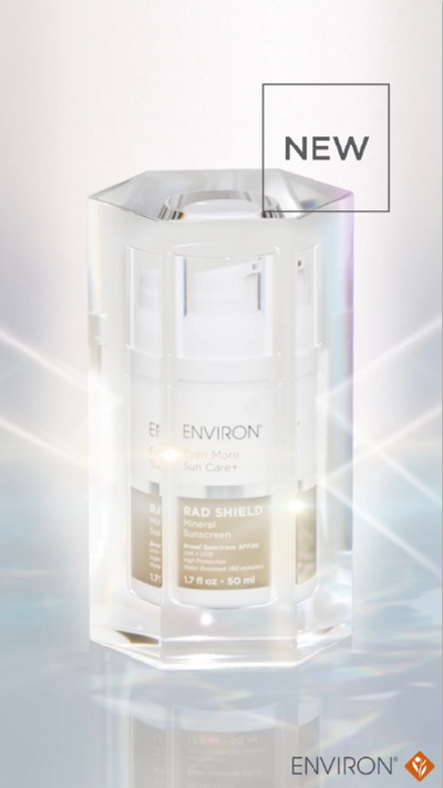 A sleek, transparent octagonal crystal display case cradles a white environ radiance shield serum bottle with gold and black labeling.