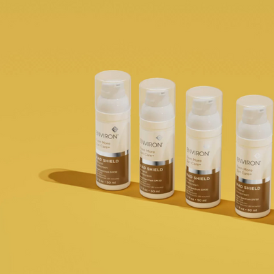 Four white and brown environ mad shield sunscreen spray bottles with clear caps, arranged in a row.
