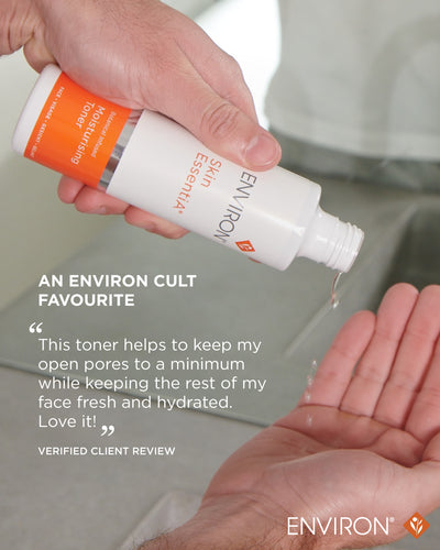 A white and orange environ skin essentia moisturising toner bottle with a silver cap, held in hand as liquid drips into an open palm.