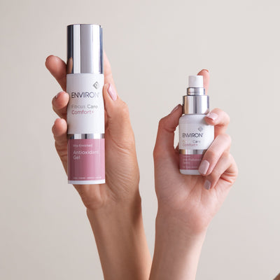 Two environ skincare products, one in a tall silver and pink bottle labeled ’focus care comfort+ vita-enriched antioxidant gel’ and the other in a smaller white and rose gold spray bottle labeled ’care comfort+’ with an anti