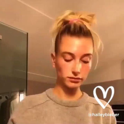 A person with blonde hair tied in a high bun wearing a gray crewneck sweater.