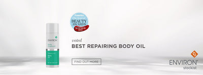 A sleek white and teal cylindrical bottle of environ body essential repairing body oil, featuring a minimalist design with clear branding.