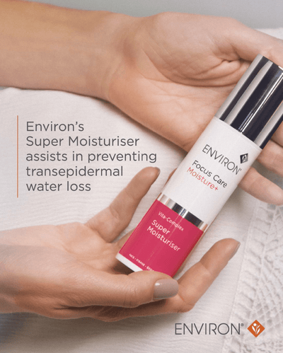A sleek white and vibrant pink cylindrical bottle of environ focus care moisture+ super moisturiser with a silver cap, held gently in two hands.