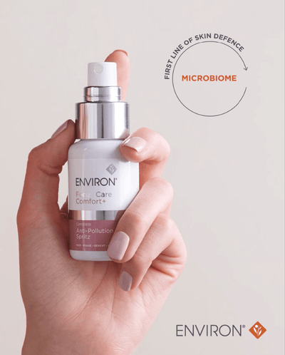A sleek white and silver spray bottle of environ firm care comfort+ complete anti-pollution spritz, held gently in a hand with light pink nail polish.