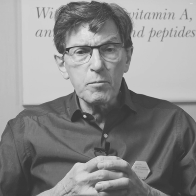 A man wearing black-rimmed glasses and a dark button-up shirt with his hands clasped in front of him.