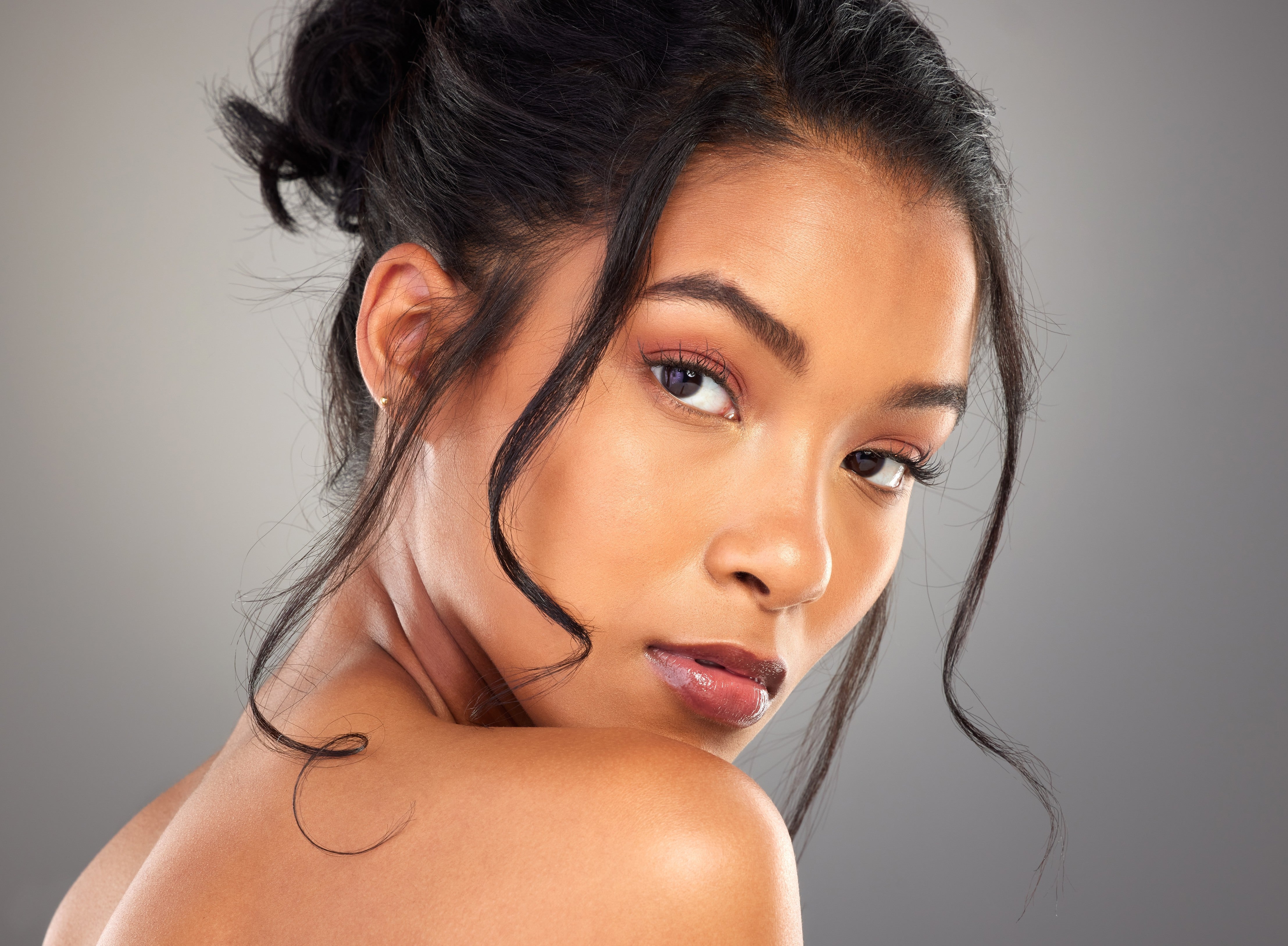 A woman with dark, wavy hair styled in a high bun and loose strands framing her face.