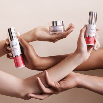 The image displays three environ skincare products: a tall cylindrical bottle with a silver cap and white label, a smaller jar with a clear glass body and metallic lid, and another similar tall cylinder.