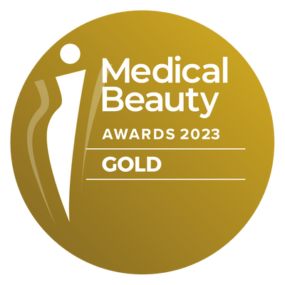 Gold-colored circular award badge featuring the text ’medical beauty awards 2023’’ and ’gold,’ with a stylized white silhouette of a person on the left.